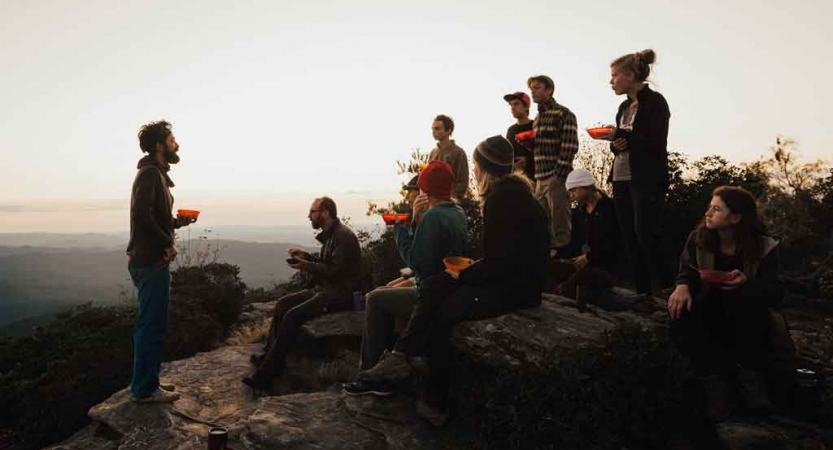 an instructor speaks to a group of students while they eat breakfast on a backpacking trip in north carolina